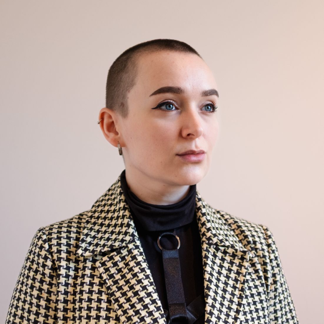 Kristin Skårdal Portrett av kortklippet kvinne med blå øyne, ikledd sort høyhalset genser og dressjakke i dog-tooth mønster